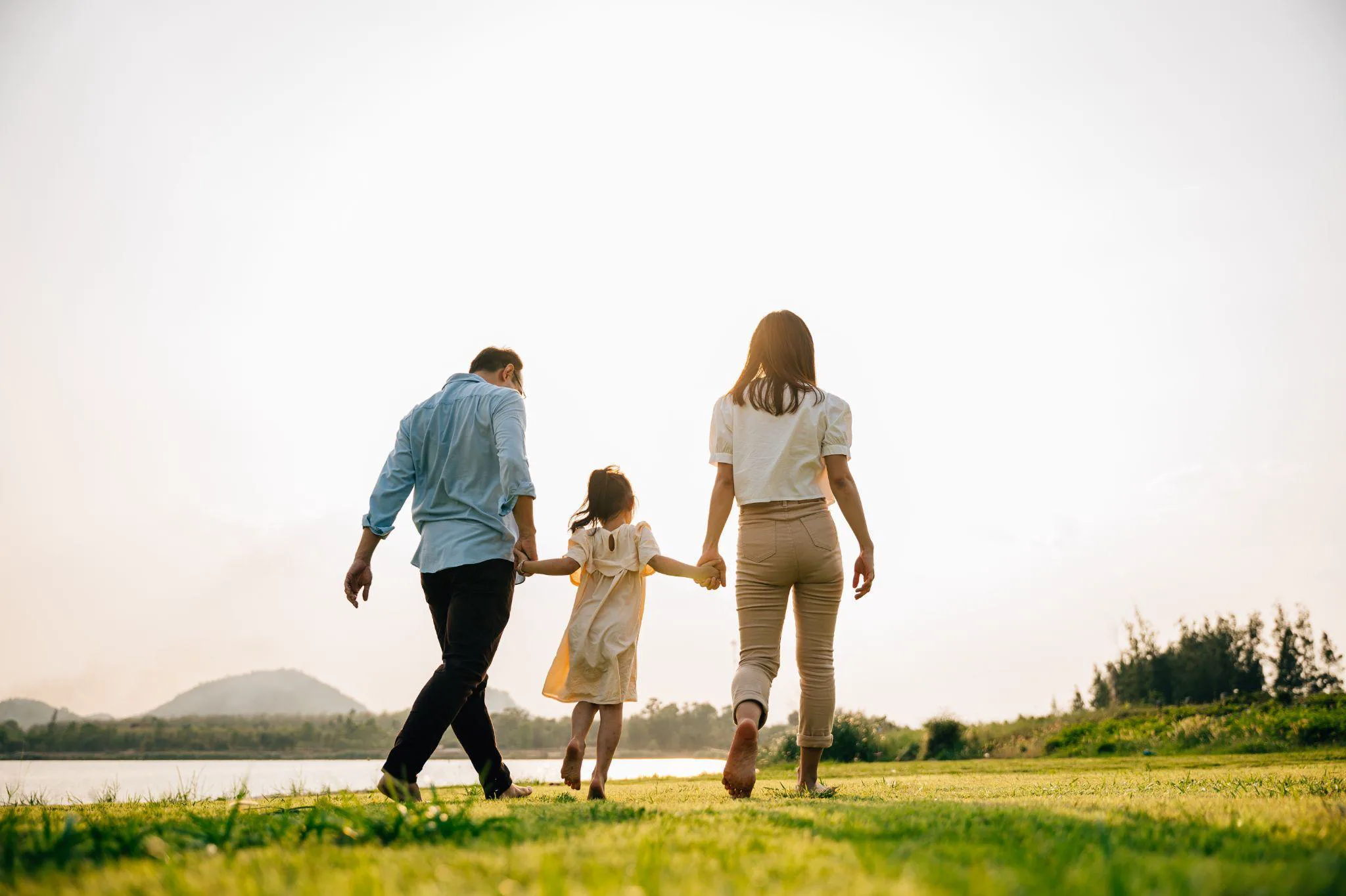 A father, mother and daughter walking hand in hand by a lake